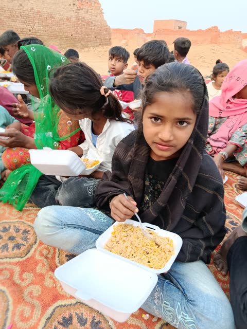 A girl looks up from her box of rice during a shared meal on a rug
