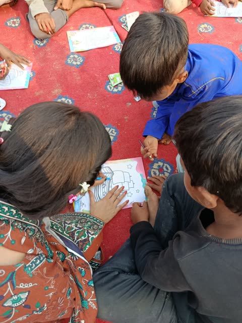 A team member helps two young boys color a picture of a ship on a red rug