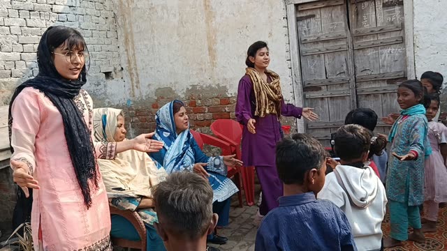 Women singing with arm motions as children face them outside a doorway