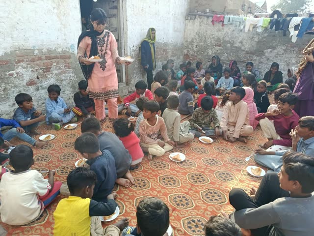 Woman carrying plates among children eating in a courtyard