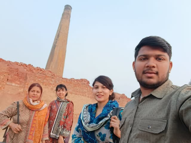 Four team members smile for a photo in front of a brick kiln chimney