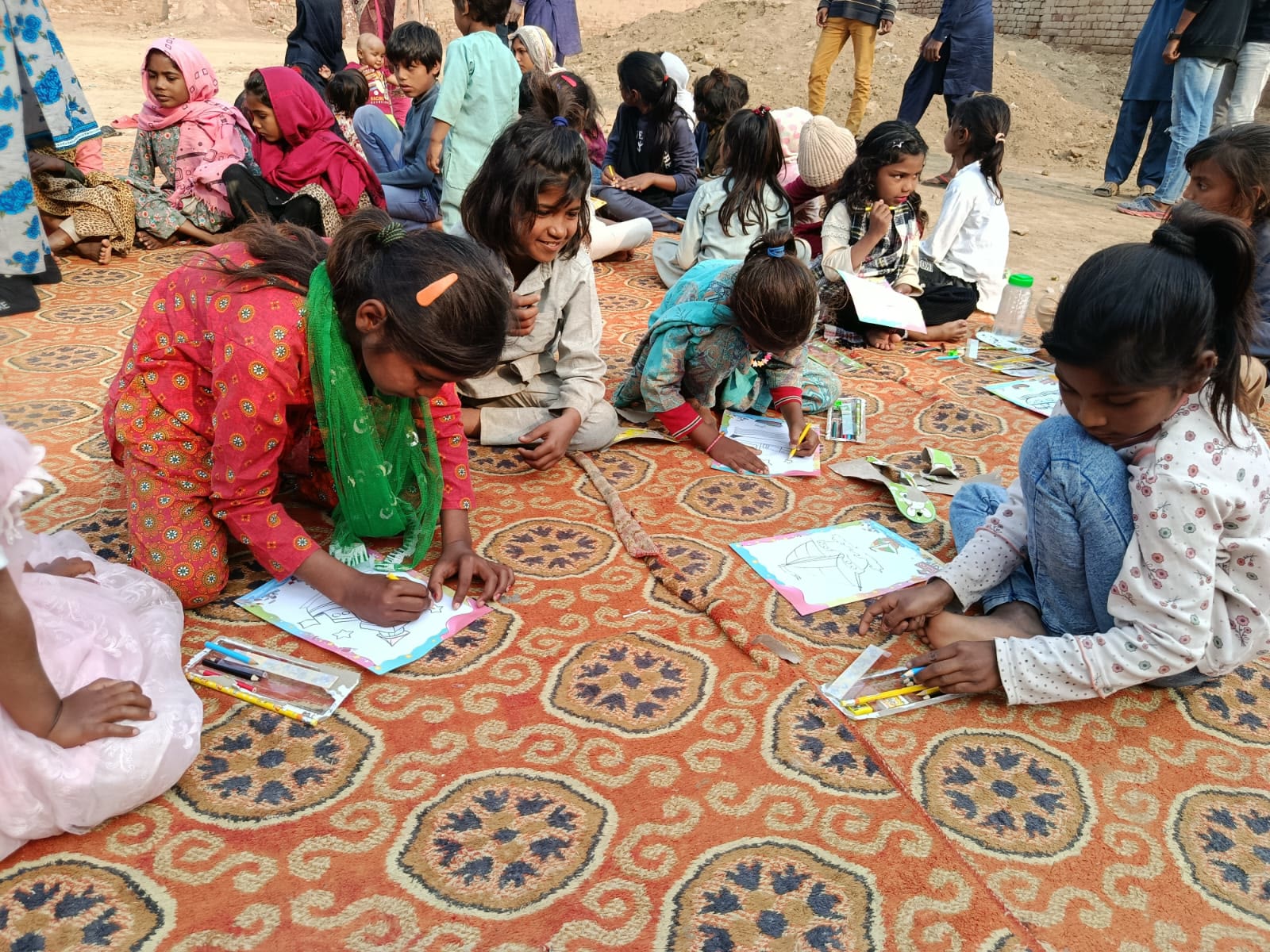 Children coloring pictures with pencils on a patterned rug outdoors