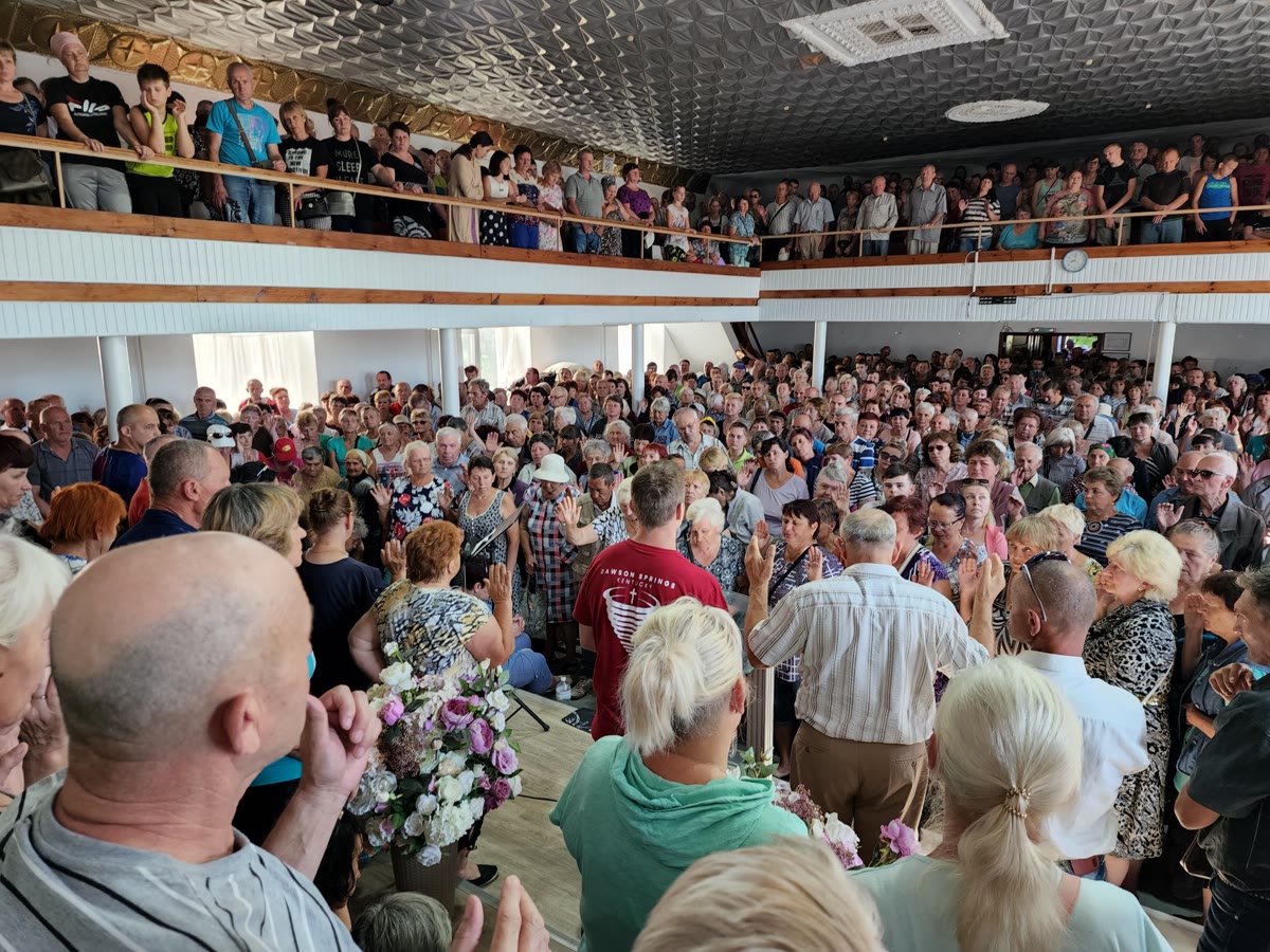A crowded hall in Ukraine with hands raised in prayer
